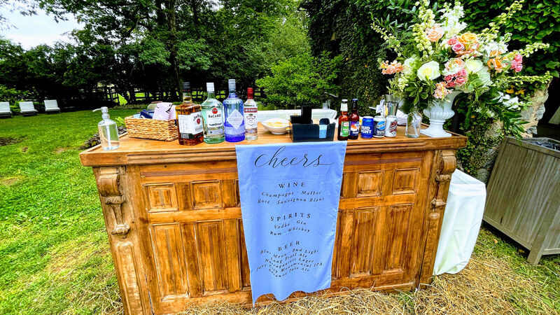 Outdoor wedding cocktail hour bar with bottles and florals