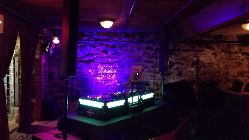 DJ performing at a bar with crowd dancing in low ambient lighting