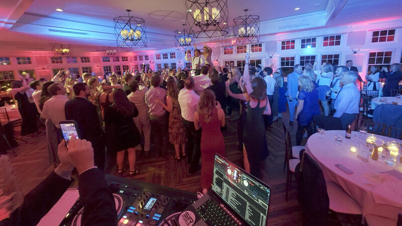 Packed wedding dance floor during a peak dancing moment with colorful uplighting