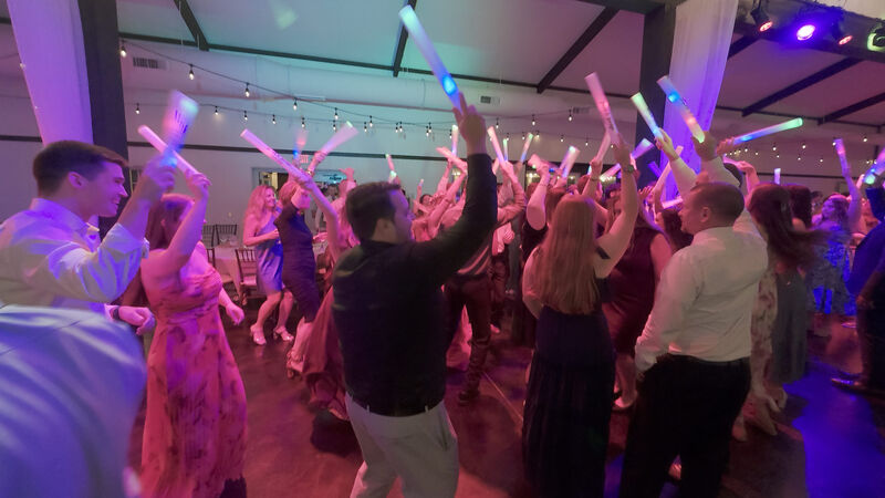 Packed wedding dance floor with guests holding LED foam sticks under colorful lighting