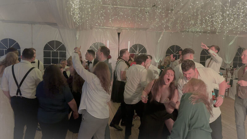 Wedding guests dancing and singing along under string lights on a packed dance floor