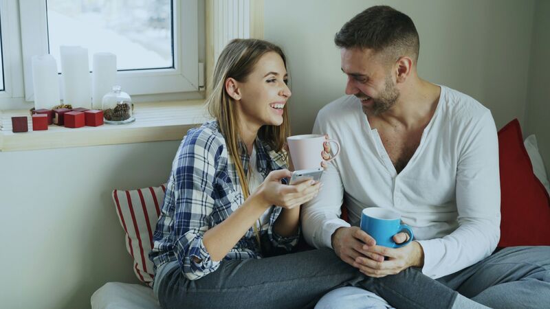 Couple laughing together over coffee at home while looking at a phone