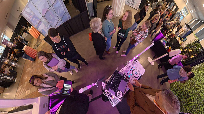 View from the DJ booth at a bridal expo with couples browsing vendor booths and purple uplighting