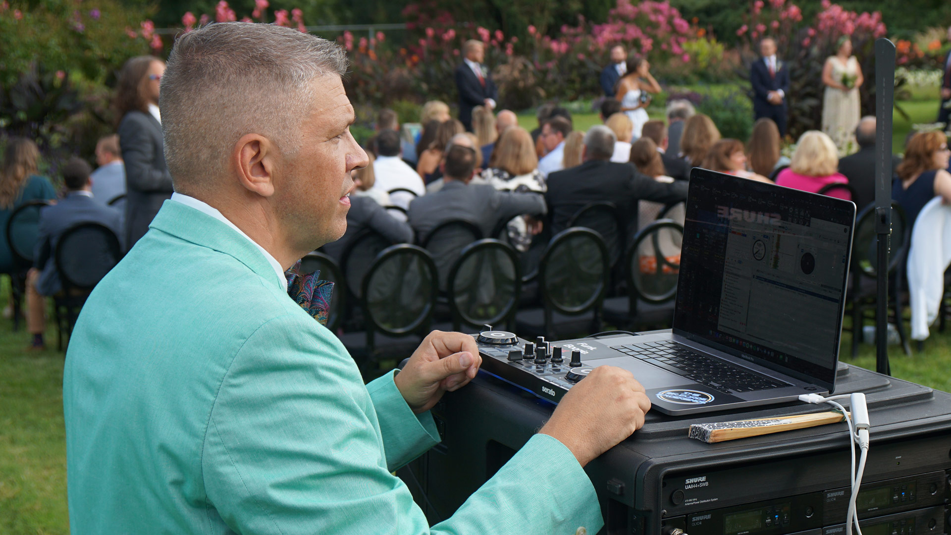 DJ operating wireless audio system at outdoor garden wedding ceremony